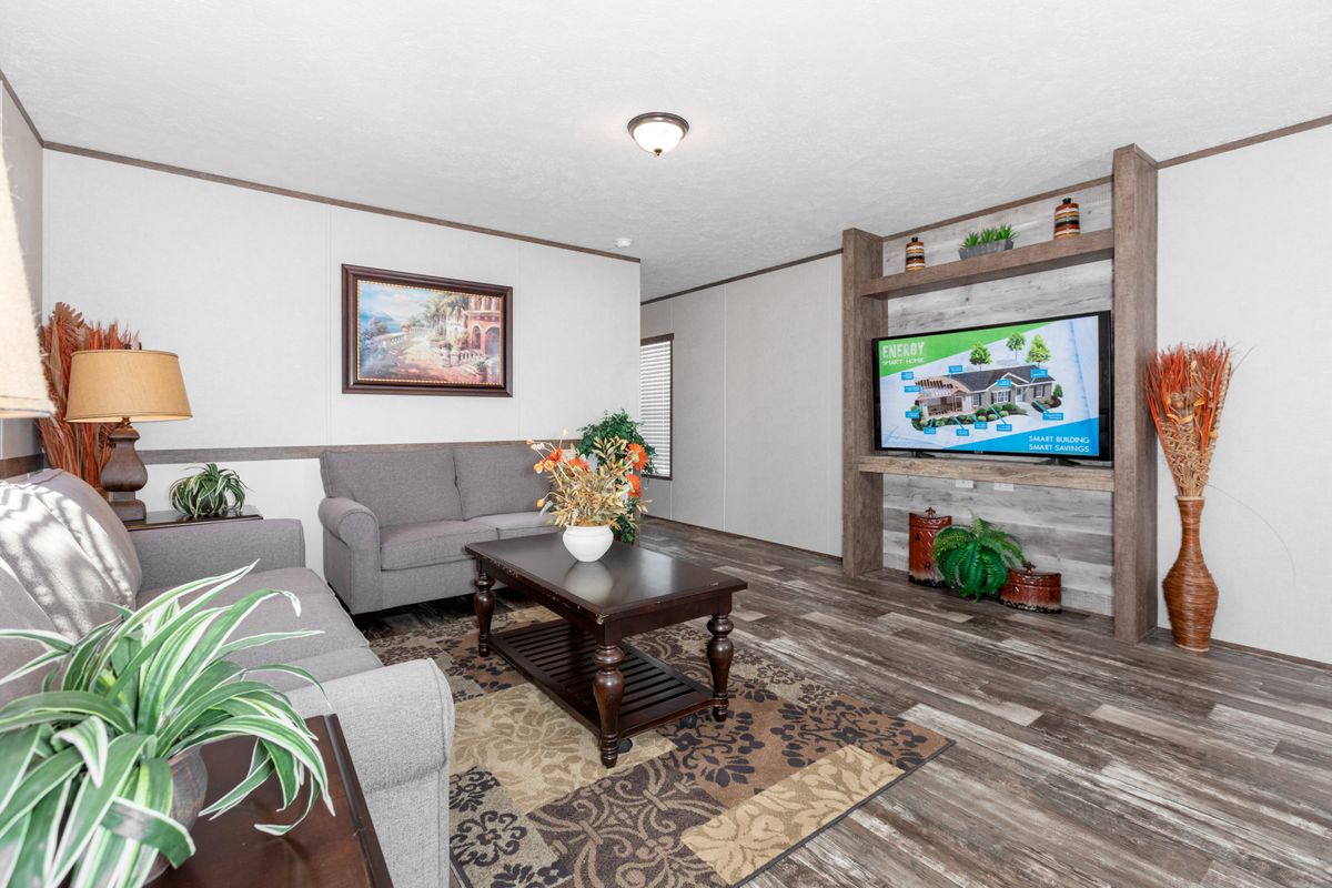 A living room in a mobile home with hardwood floors and a tv.