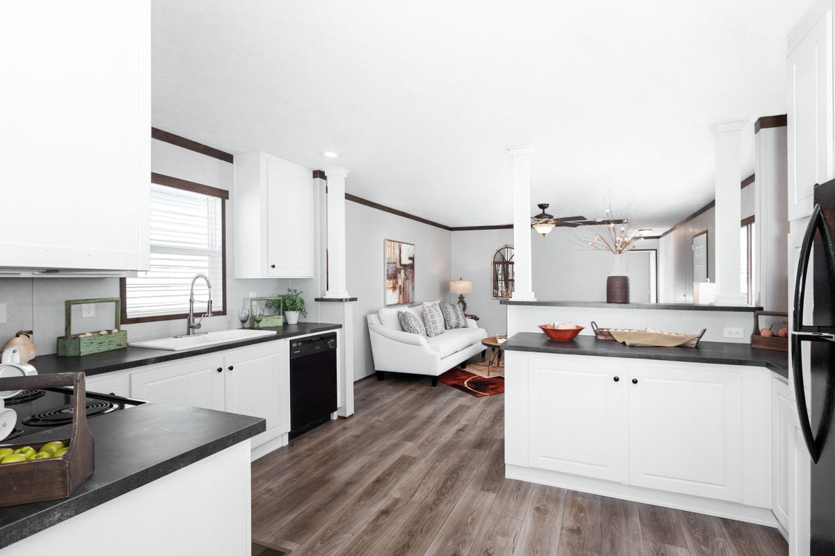 A white kitchen with black appliances and wood floors.