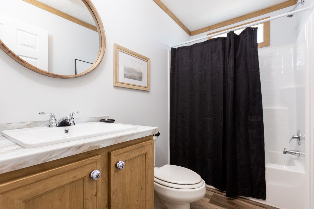 A bathroom with a black shower curtain and wooden floors.