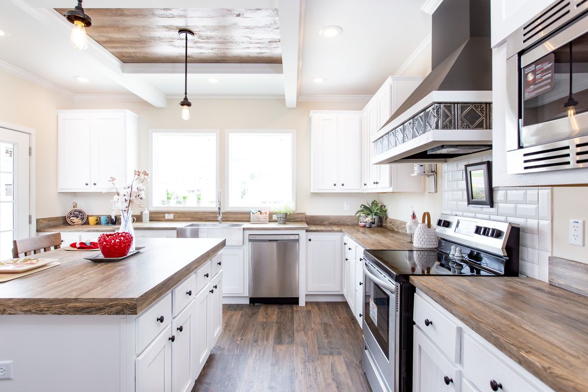 3027866d-d401-4073-8080-b6923e50944c A white kitchen with wood floors and stainless steel appliances.