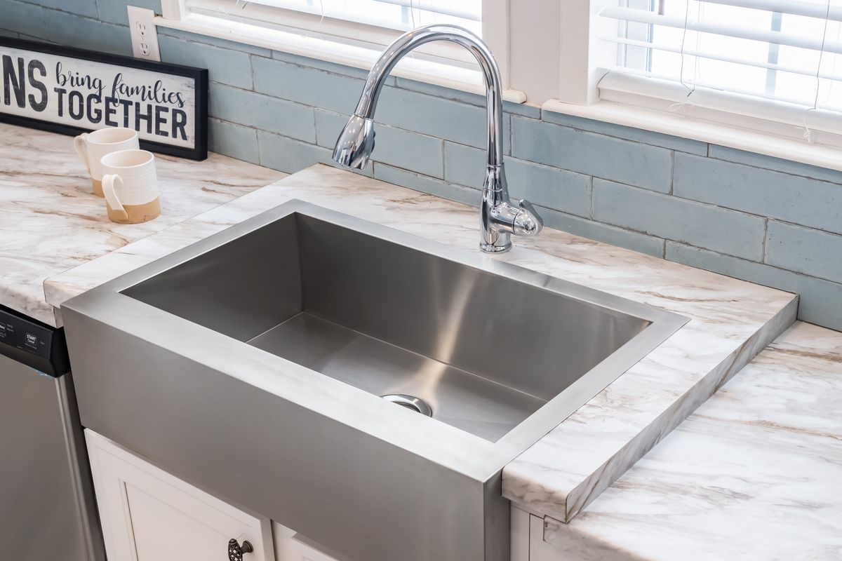 50bb0335-e5ea-43f5-b8b8-696fe7822b38 A stainless steel sink in a kitchen with marble counter tops.