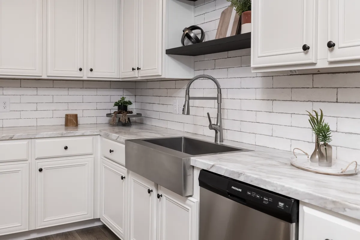 5e1f1120-0c69-4d06-b6b2-86efd08cb09a (1) A kitchen with white cabinets and a stainless steel sink.