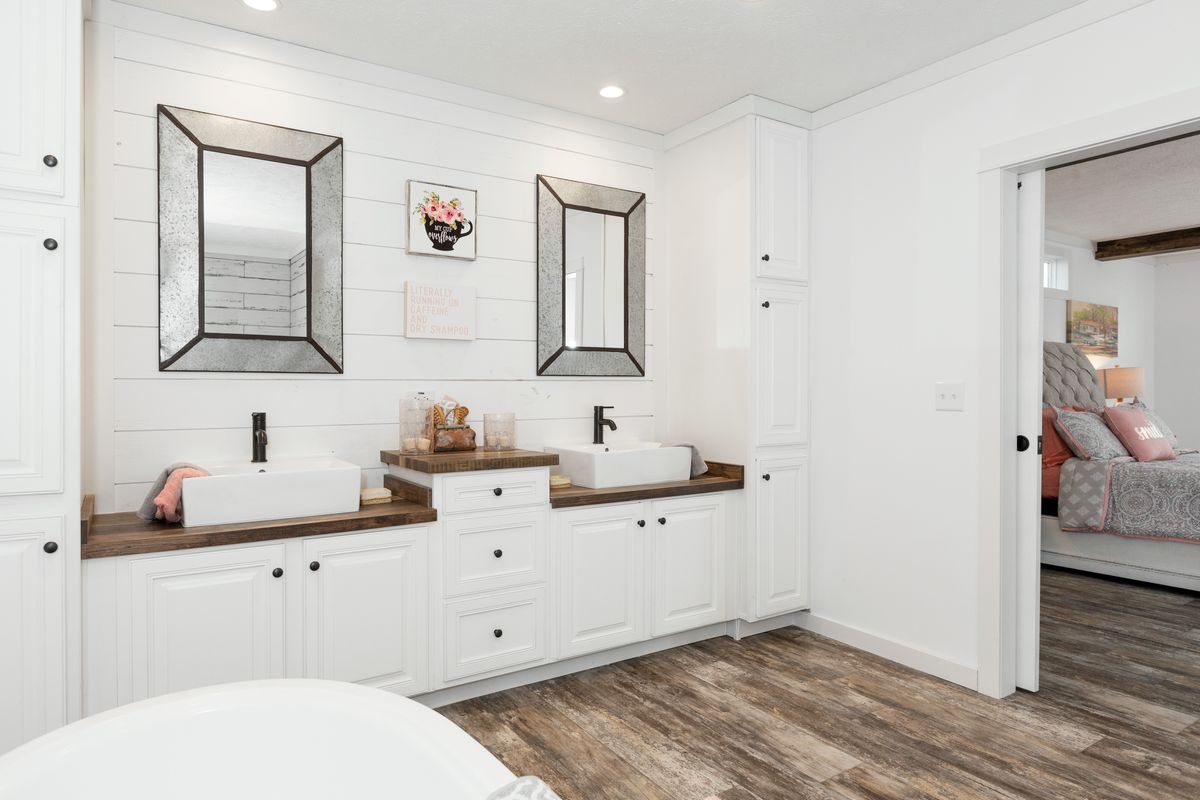 A bathroom with white cabinets and wood floors.