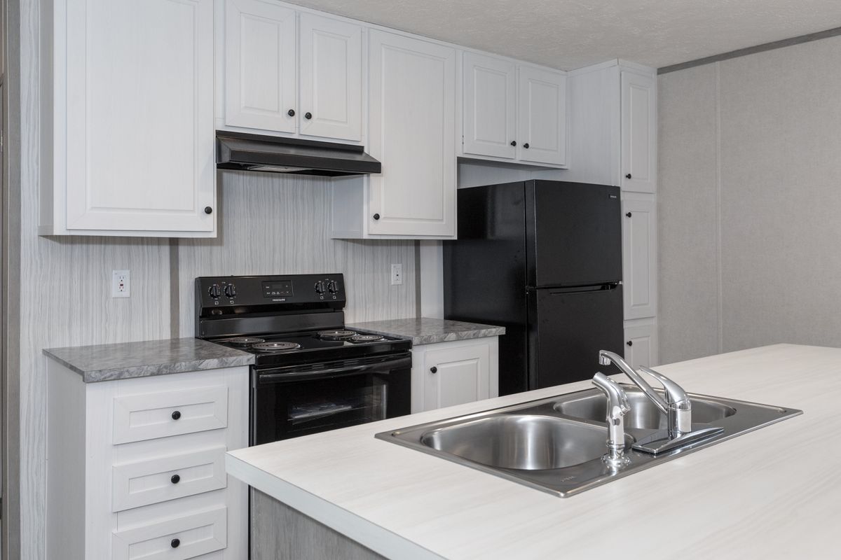 7acda514-40a9-44bd-a450-30607a721487 A kitchen in a mobile home with white cabinets and stainless steel appliances.