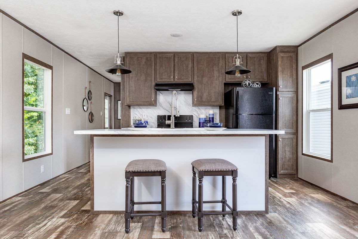 81be057d-a54a-44d4-869a-c94ca0fed1a9 A kitchen in a mobile home with wood floors and stools.
