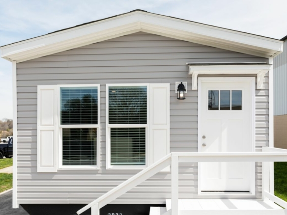 A small gray mobile home with a white front door.