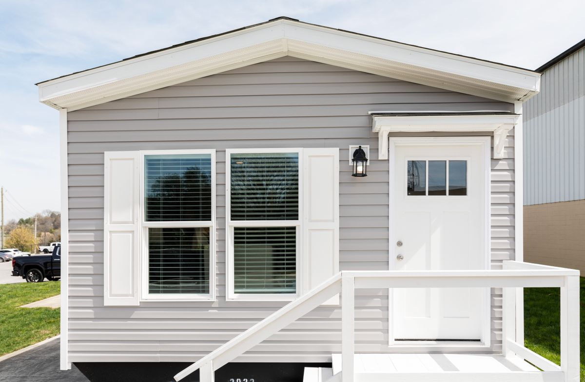 824e3fc0-e46c-43cc-bda7-8ccfb05b799f A small gray mobile home with a white front door.