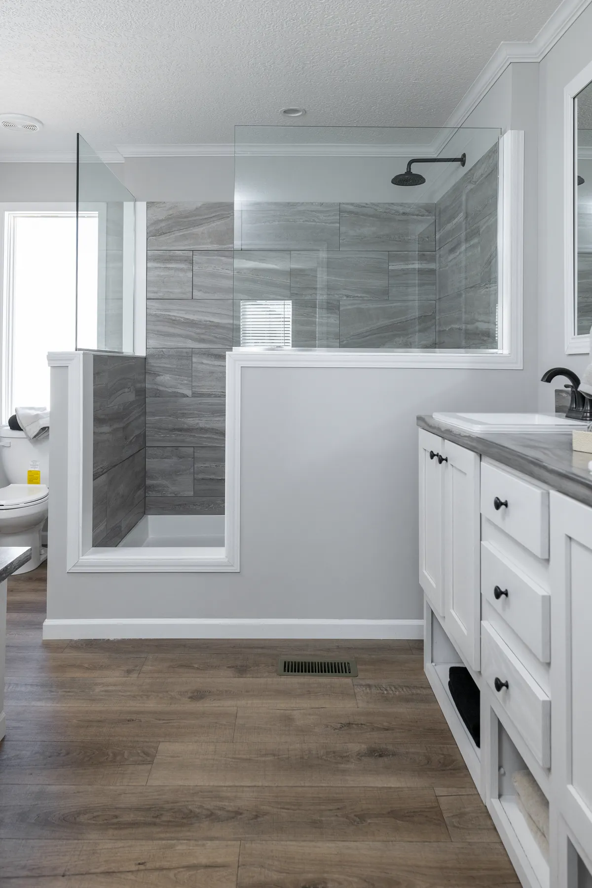 A white bathroom with wood floors and a glass shower.