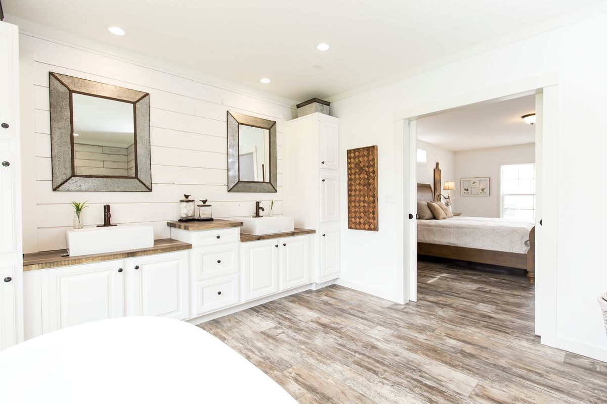 A white bathroom with wood floors and white cabinets.