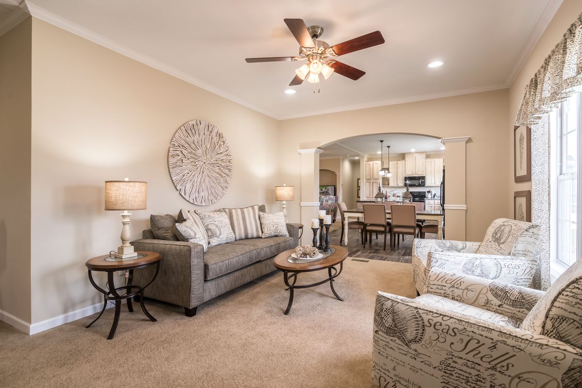 A living room with a ceiling fan and beige furniture.