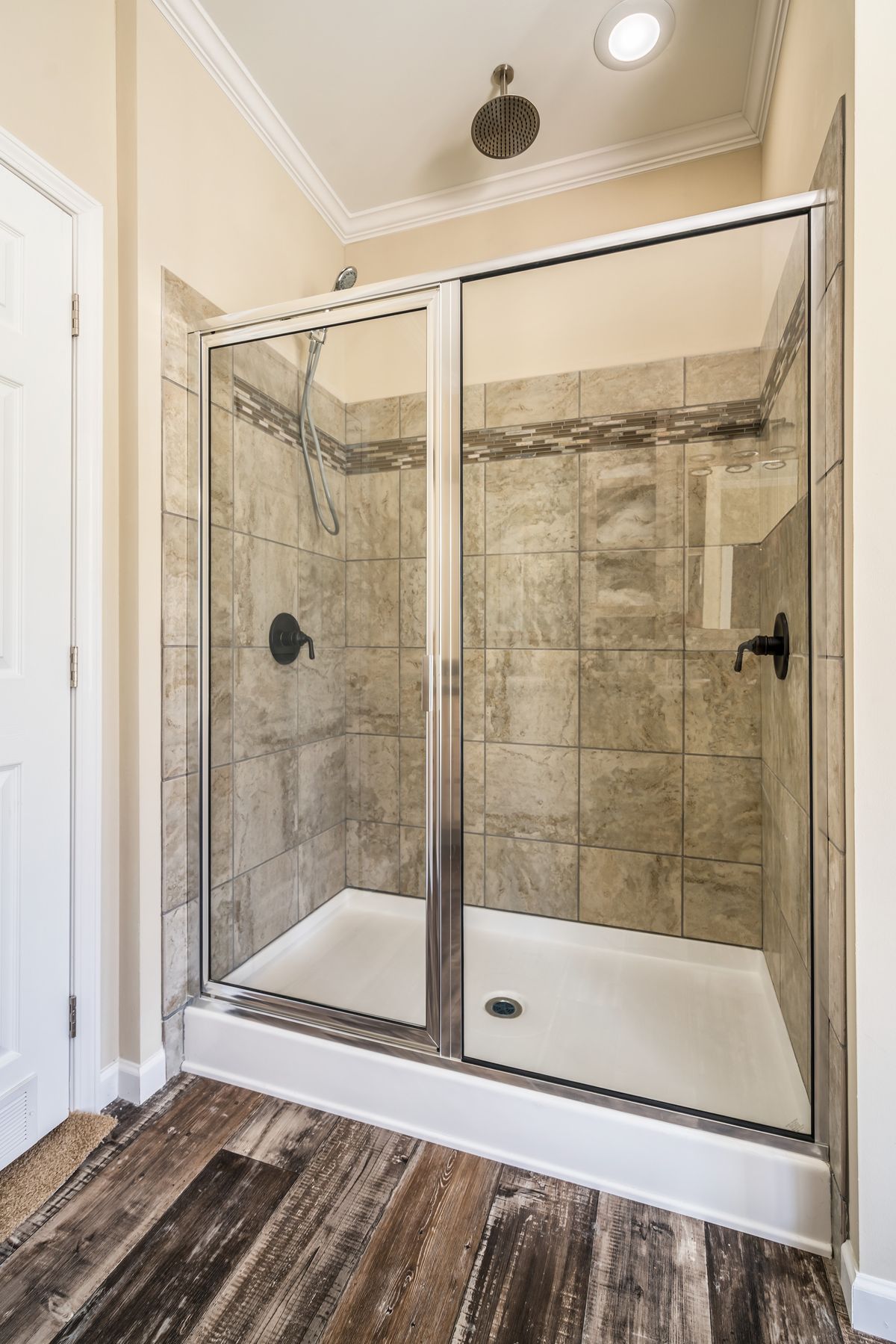 A bathroom with a glass shower door and wood floors.