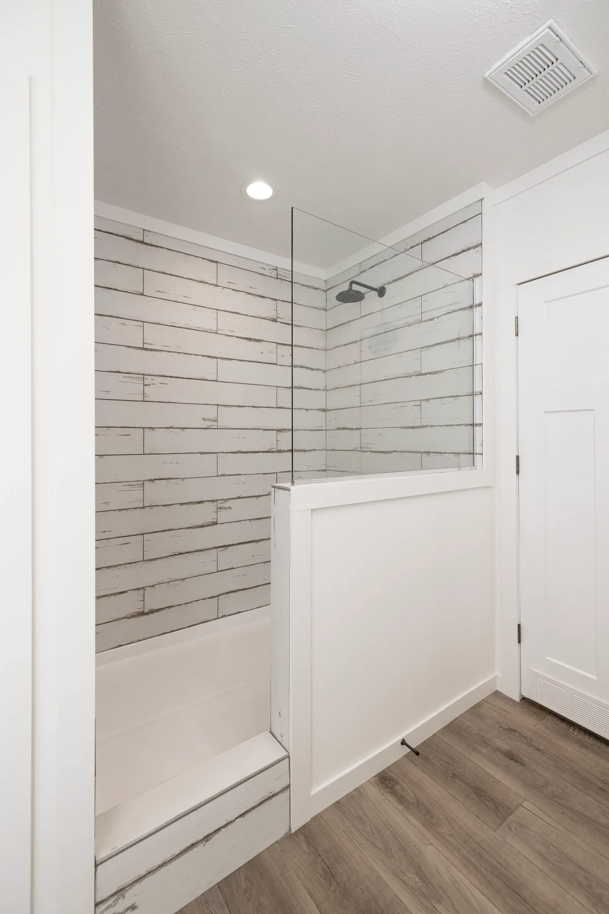 bd04baef-2bae-4404-bc46-d10ad48d6dc1 A white bathroom with wood floors and a glass shower.