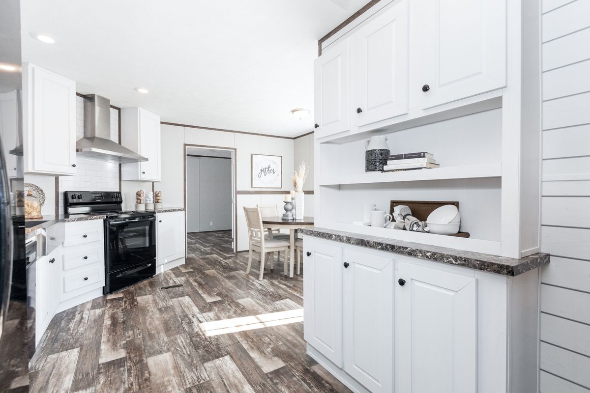 A mobile home kitchen with white cabinets and wood floors.
