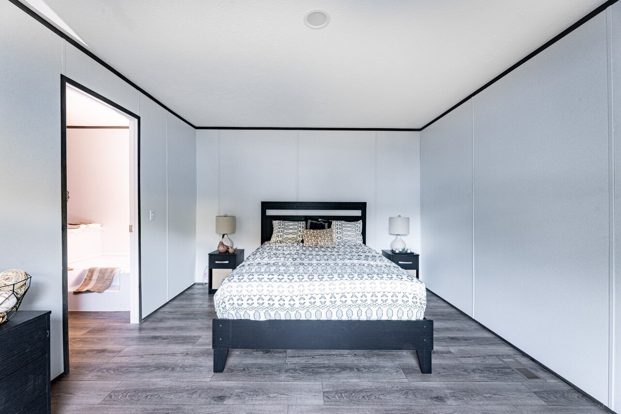 A bedroom in a mobile home with white walls and wood floors.