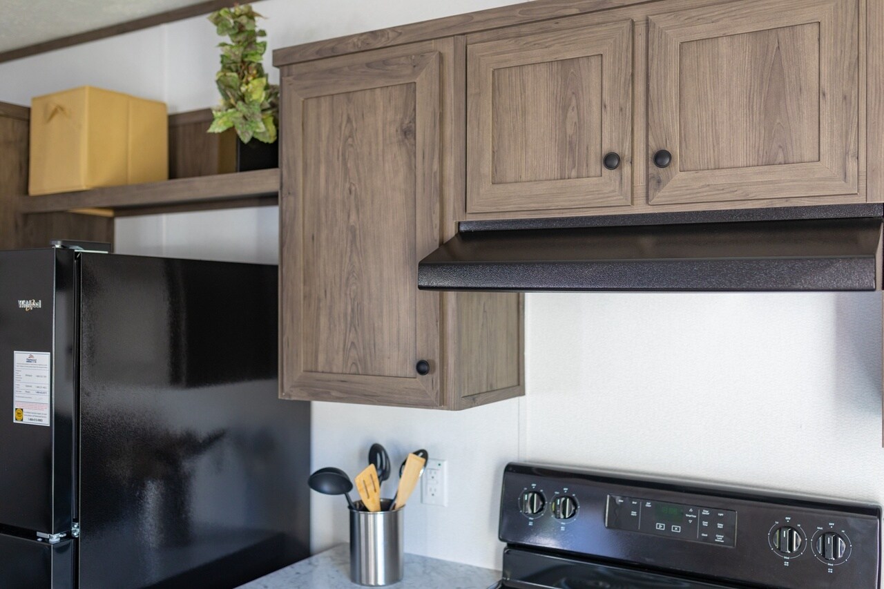 A kitchen in a mobile home with wood cabinets and black appliances.