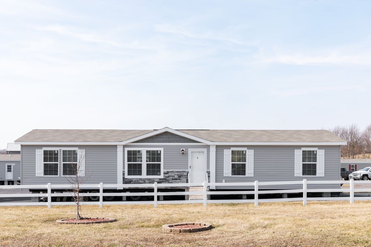 ccd83878-5a0e-47de-bad0-67dfc8daf52f A gray mobile home with a white fence.