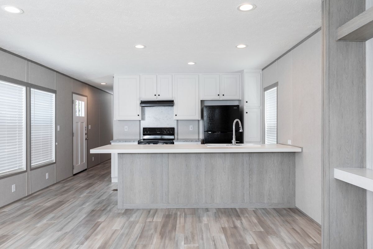 d7969cc5-094c-4e9b-b26c-a746e76f9669 A kitchen in a mobile home with white cabinets and wood floors.
