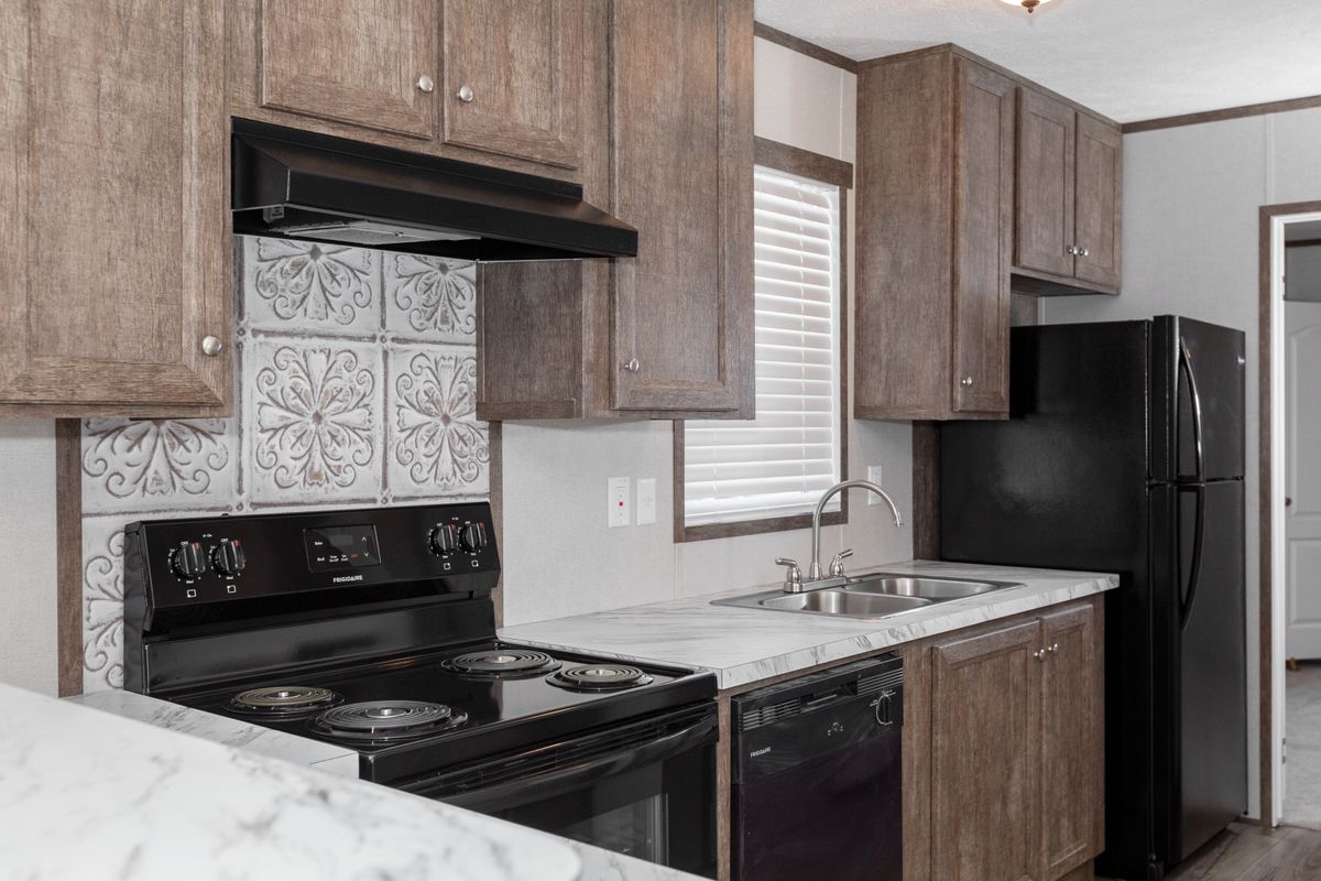 d90e05cd-3779-4b31-90ce-f309f5d90135 A kitchen in a mobile home with wood cabinets and black appliances.