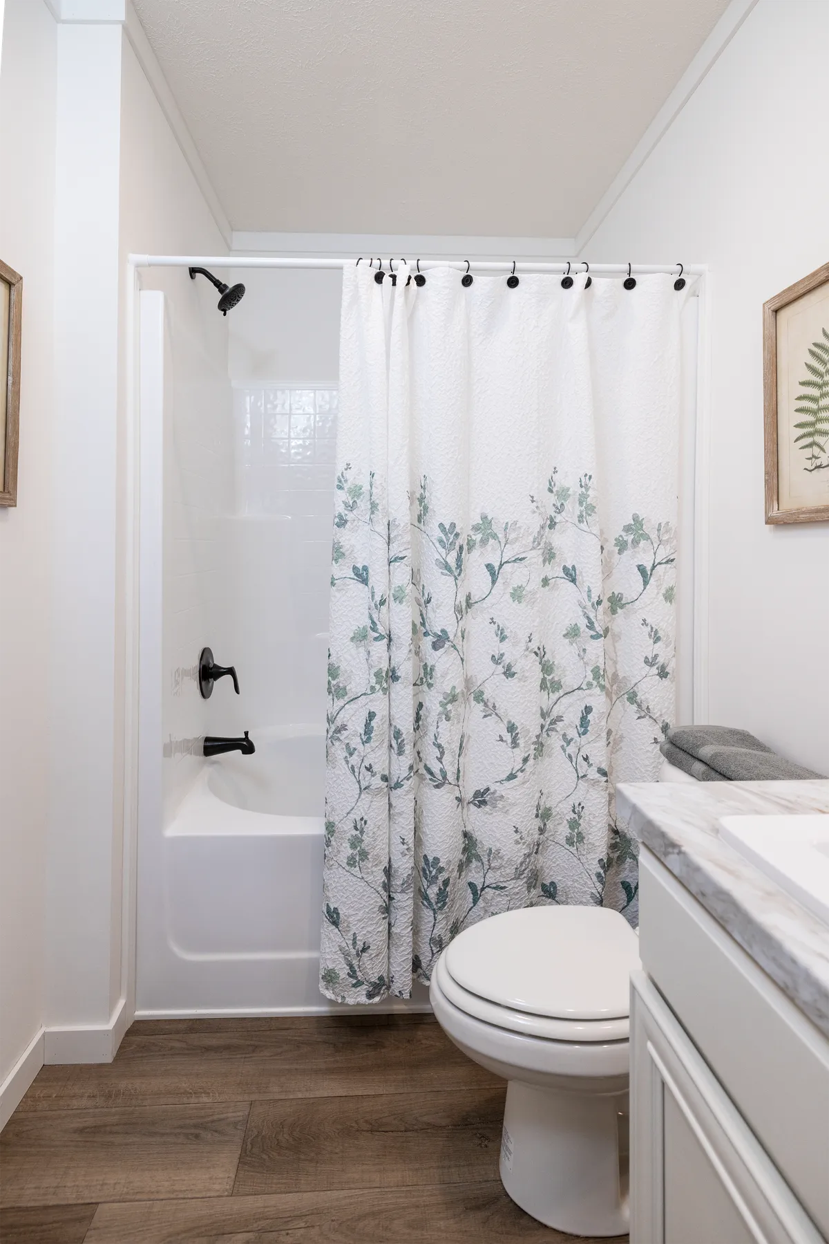 e2b26ea5-8bba-4077-bdc5-fd0307644063 A bathroom with a white shower curtain and wood floors.