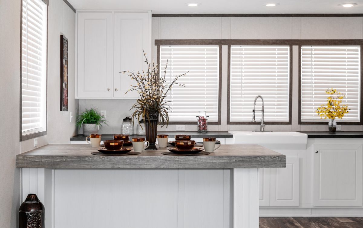 A kitchen in a mobile home with white cabinets and wood floors.