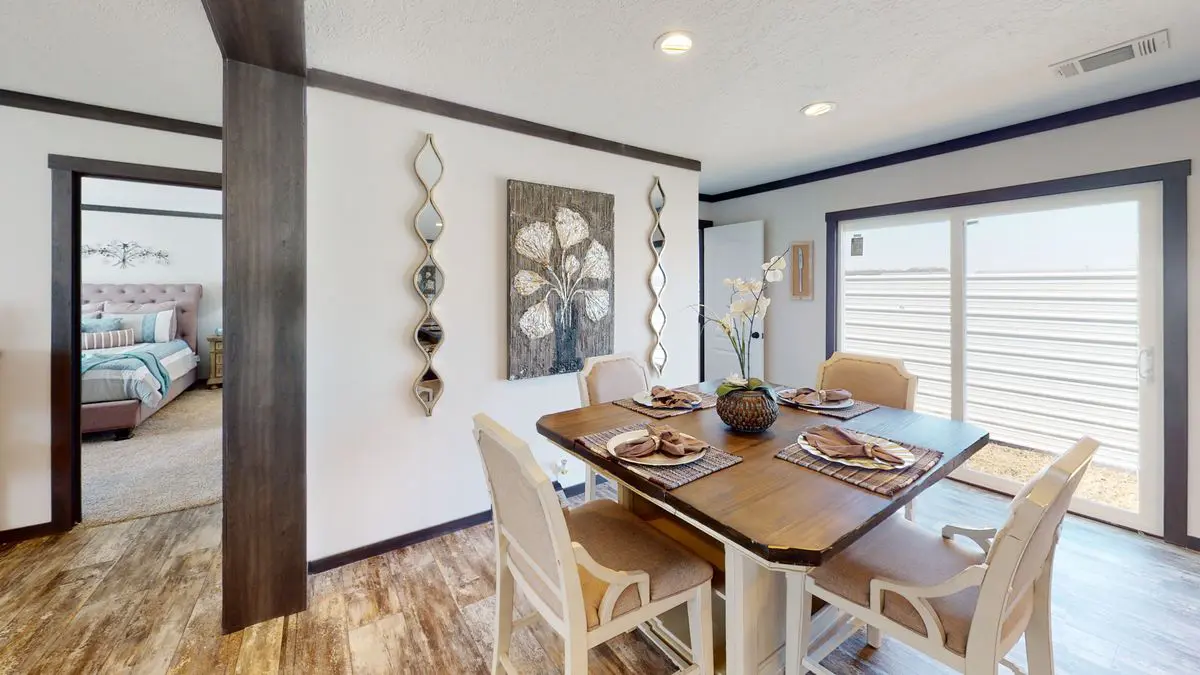 0fc2e3fc-310a-40d7-988d-40f50f26ff4b Modern dining room with a wooden table set for four, decorative wall art, and an open view into a bedroom. bright natural light streams in from large glass doors.
