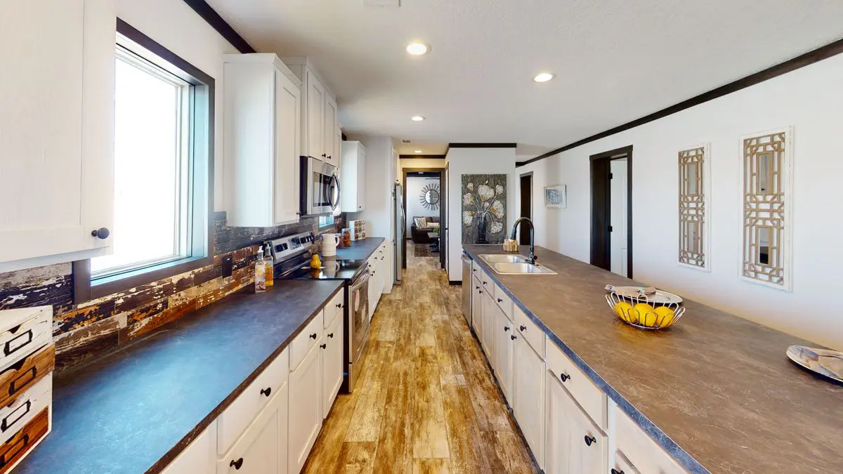 1f49fd2c-372e-4b0a-b3a4-292790c88ffe A modern kitchen with long countertops, white cabinets, and wooden floors, leading to a hallway with decorative mirrors on the wall.