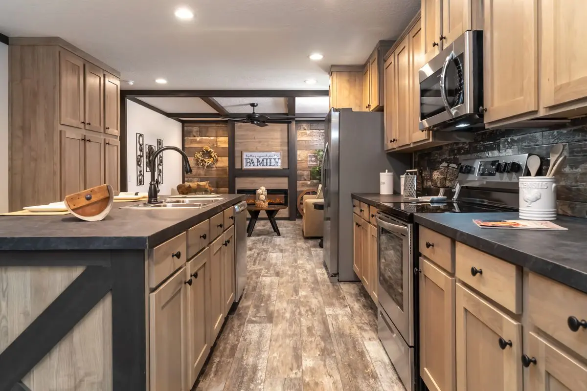 A modern kitchen with wooden cabinets, black countertops, stainless steel appliances, and a central island.