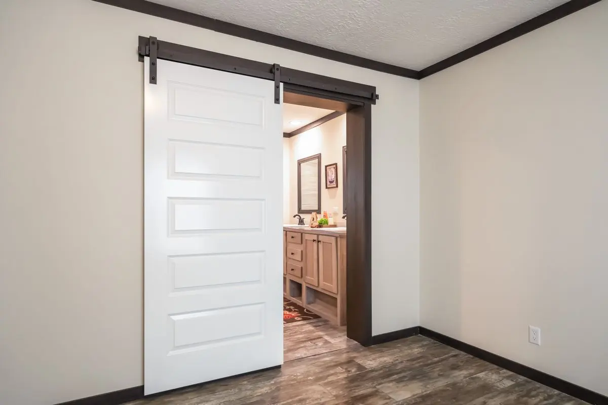 A modern sliding barn door, partially open, leading to a bathroom with wooden cabinetry and tiled flooring.