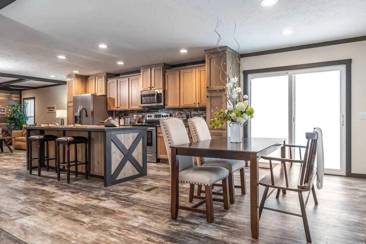 Modern kitchen interior with wooden cabinetry, a central island with bar stools, and an adjacent dining area with a table and chairs, featuring large sliding doors.