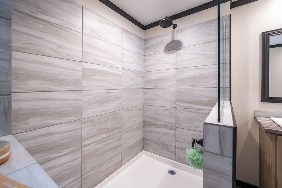 Modern bathroom with light gray marble tile walls, a rectangular white bathtub, and a minimalist black ceiling shower head.