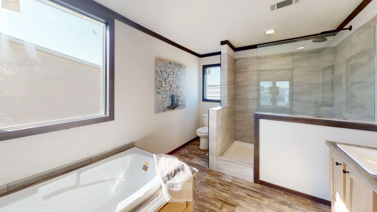 8be44d9e-3867-4391-8e01-35a4d29c7cfc Modern bathroom with a white bathtub, enclosed glass shower, single vanity, and a wall-mounted artwork. brightly lit, with beige walls and dark trim.