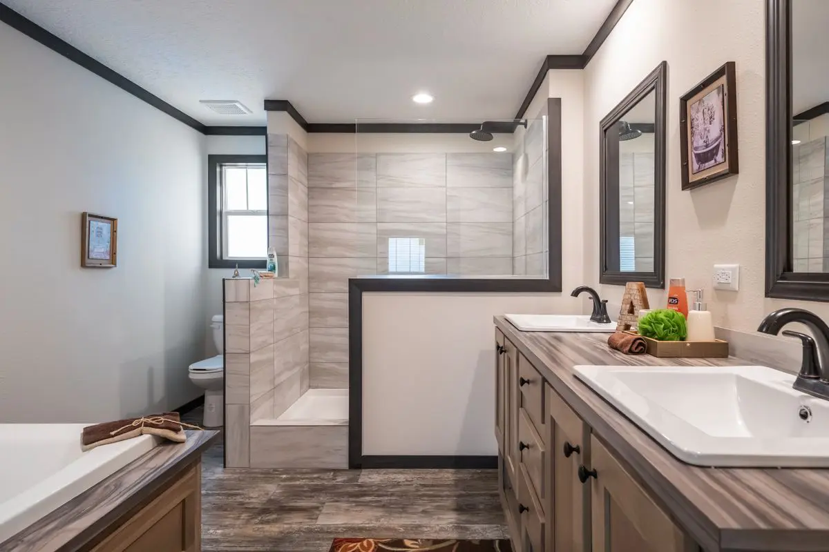 Modern bathroom with dual sinks, dark cabinets, and a glass-enclosed shower, featuring gray tiles and wooden flooring.