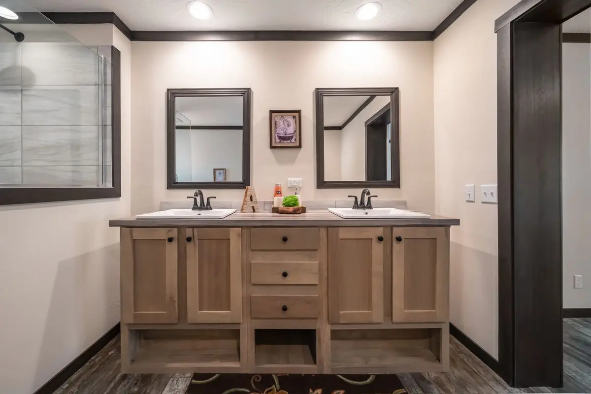 A modern bathroom vanity with twin sinks, large mirrors, and wood cabinets in a room with beige walls and dark trim.