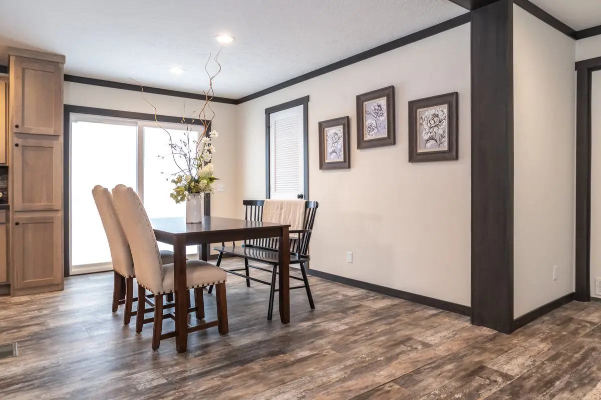 Modern dining room with a wooden table, four chairs, framed art on the walls, and a wooden cabinet, featuring dark floors and grey walls.