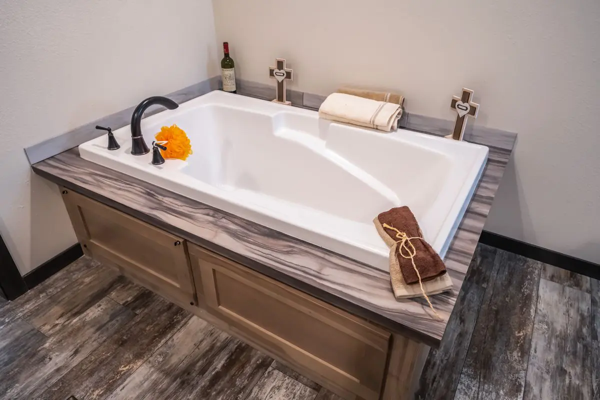 Modern bathroom featuring a rectangular bathtub with black fixtures on a wooden vanity, decorated with towels and a flower.