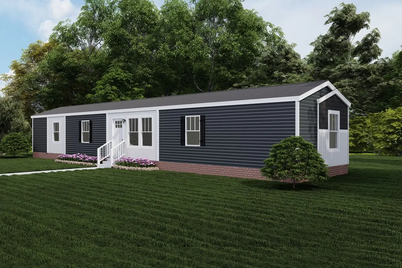 Baby-Boujee-fa5fb22f-9a83-4c14-9c4c-87177c7eef7e A single-story, dark-colored mobile home with white trim, situated on a neatly manicured lawn, is surrounded by trees. A small set of white stairs leads to the front door.