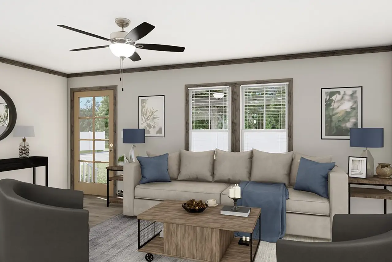 Living room with a beige sofa adorned with blue pillows, a wooden coffee table, a ceiling fan with lights, and large windows with blinds. Decor includes framed pictures, lamps, and natural light.