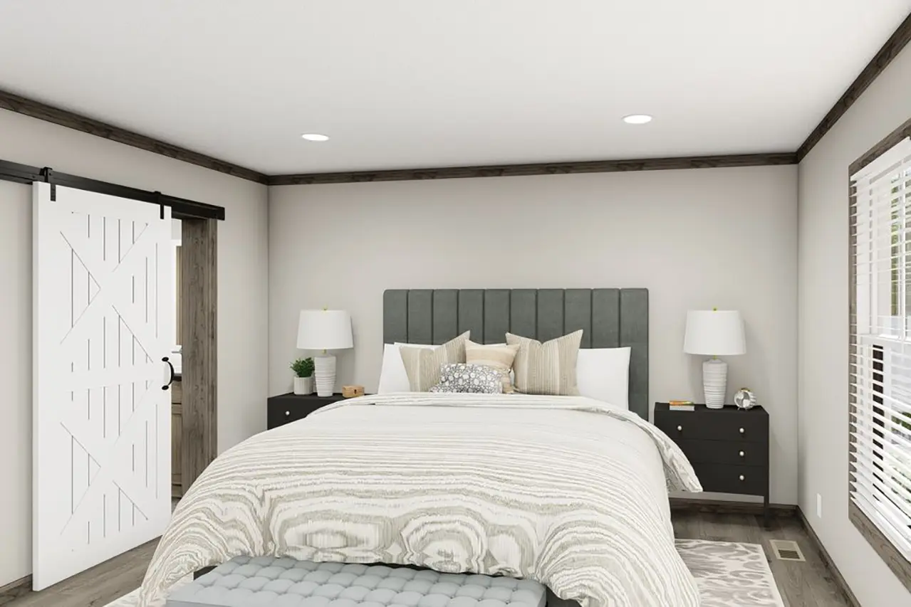 A modern bedroom with a bed featuring a padded headboard, gray and white bedding, and pillows. Two bedside tables with lamps are on either side, and a sliding barn door is on the left.