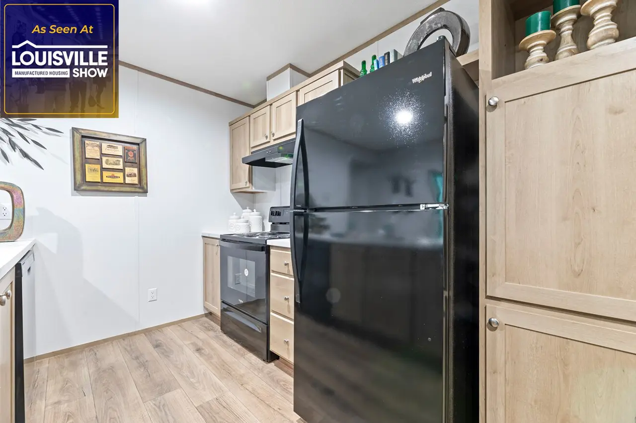 A kitchen with light wood cabinets, black refrigerator, stove, and microwave. A "As Seen At Louisville Manufactured Home Show" sign is visible in the corner.