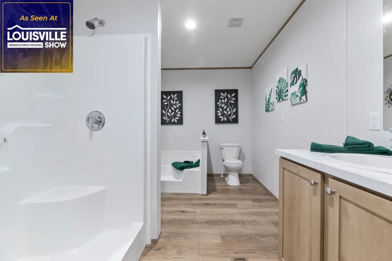 Modern bathroom featuring a walk-in shower, wood flooring, a toilet, a white bathtub with green accents, and framed artwork on the walls. A sink with a wooden cabinet is on the right side.