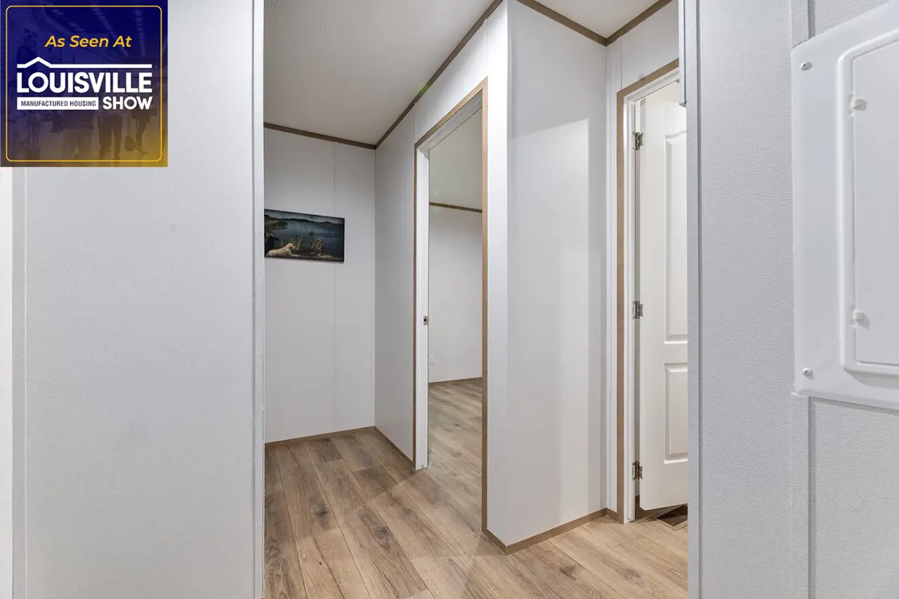 A hallway with white walls and wood flooring, featuring partially open white doors leading to different rooms and a framed picture on one wall. A "Louisville Show" sign is in the top left corner.