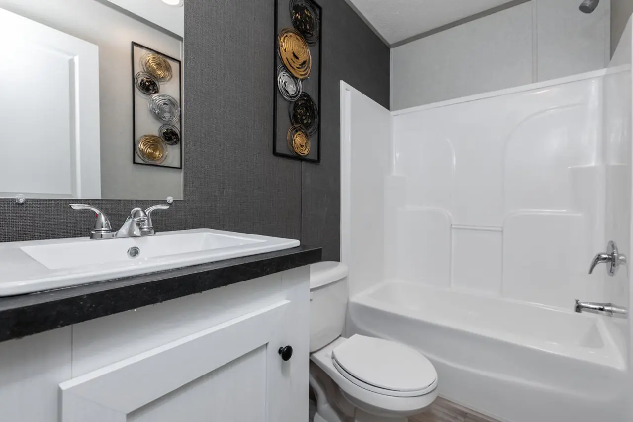 7ebe3ed2-a20b-4e52-9260-661b42ad1bae Modern bathroom with dark gray walls, white fixtures, and a bathtub. Wall art with circular designs above the toilet.
