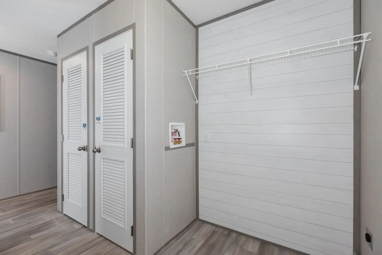 920a6430-f880-4c33-b8af-925307998077 Empty room with wood-textured floor, two closed white doors, and a blank wall featuring a small open shelf and wire hanging rack.