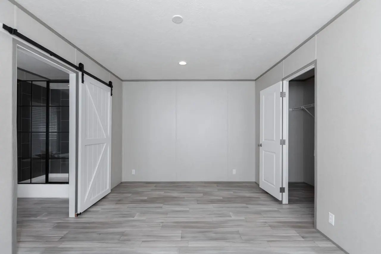 b0e072e0-2637-472a-af9d-b5ab48498527 Empty room with gray wood flooring, white walls, ceiling light, and two sliding barn doors beside an open closet door.