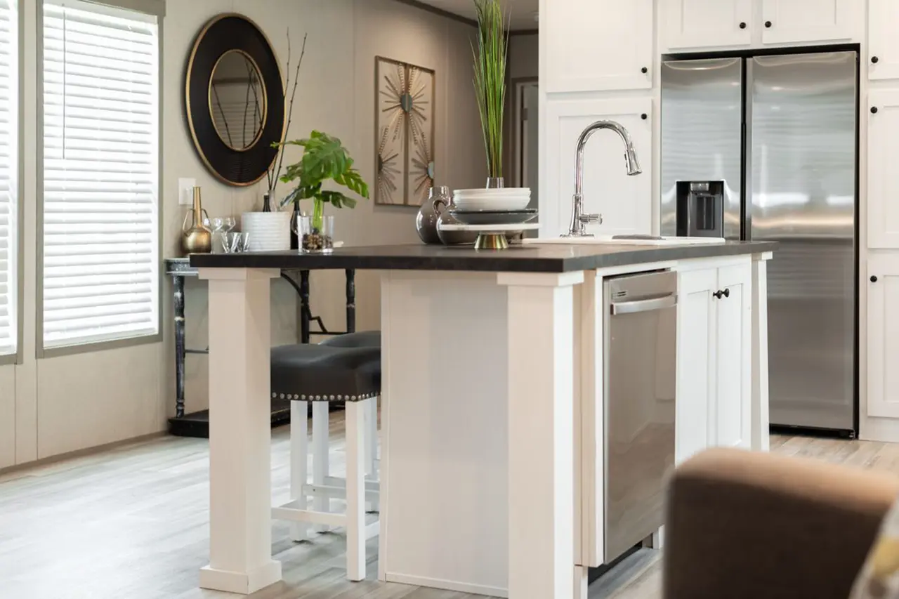 b6595ece-e033-41bd-9e0e-7f39e621f9be Modern kitchen with a central island featuring plants and decorative items. White cabinets surround stainless steel appliances, with a round wall mirror and artwork in the background.