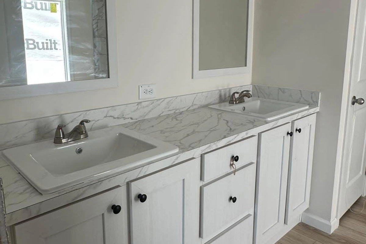 A bathroom features a double sink vanity with a white marble countertop, two mirrors, and white cabinets with black knobs.