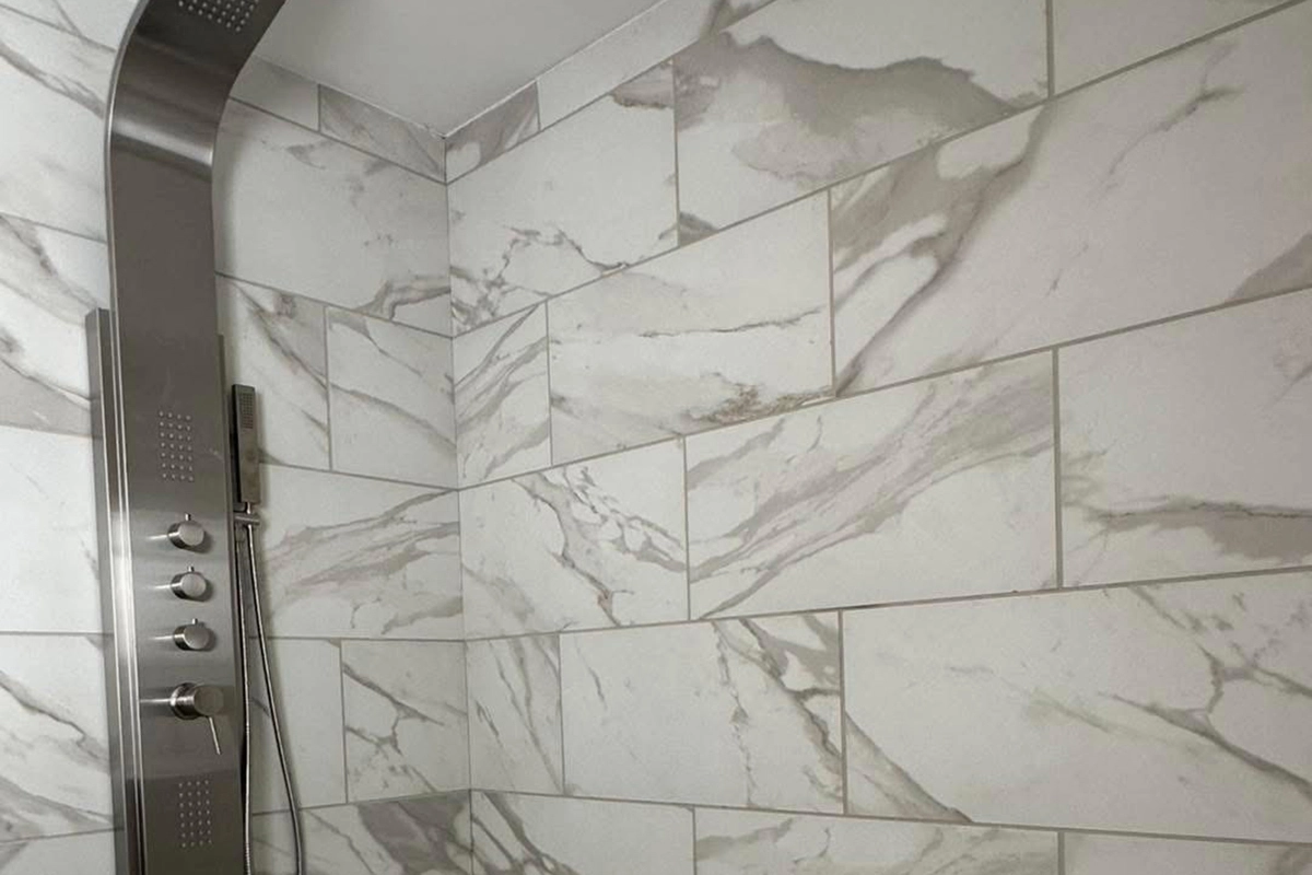 Shower with stainless steel panel and controls, featuring large white tiles with gray marble veining on the walls.
