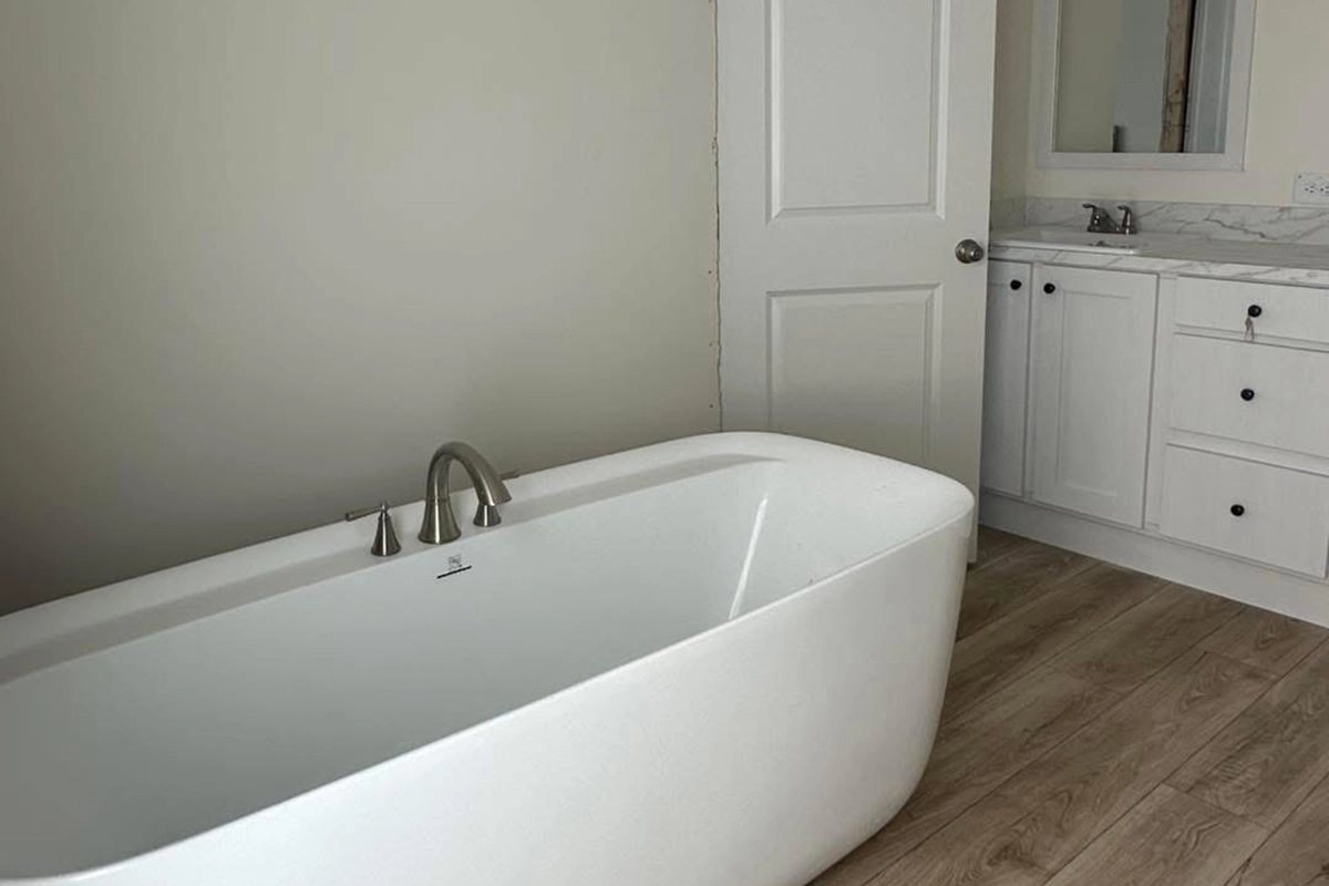 Modern bathroom with a white freestanding bathtub, light wood flooring, a white vanity with marble countertop, and a wall mirror.