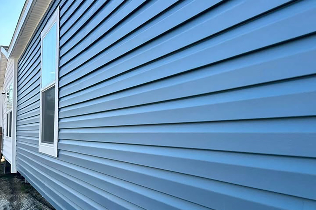 A close-up view of a house exterior featuring blue vinyl siding and a single window with a white frame.