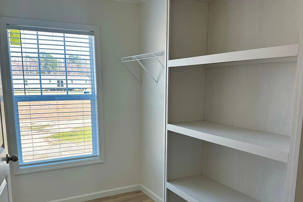A small room with a window, built-in shelves on the right, a wire rack on the left wall, and light-colored flooring.